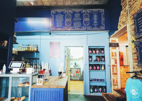 Interior of a cozy café featuring a blue color scheme, a wooden counter, and shelves with various products.