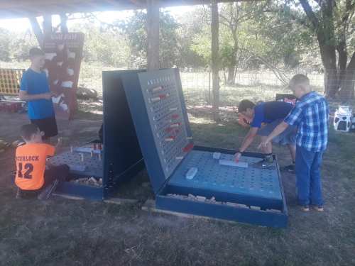 Children playing a large outdoor game resembling Battleship, with two game boards and a grassy area in the background.