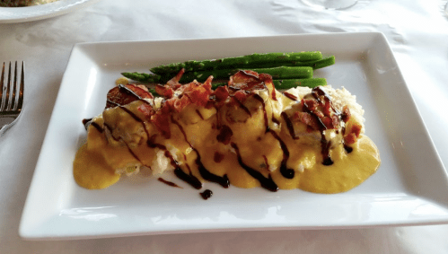 A plate of creamy pasta topped with bacon, drizzled with sauce, served with asparagus on the side.