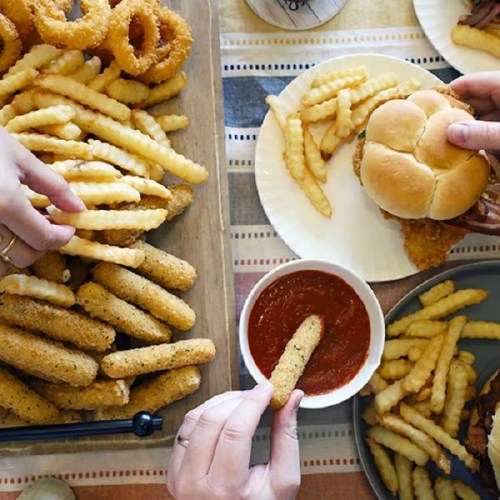 A spread of crispy fries, onion rings, and mozzarella sticks with dipping sauce, alongside a sandwich on a plate.