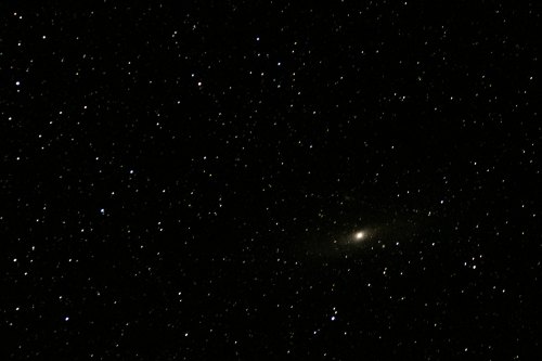 A dark sky filled with countless stars, featuring a faint galaxy in the center.