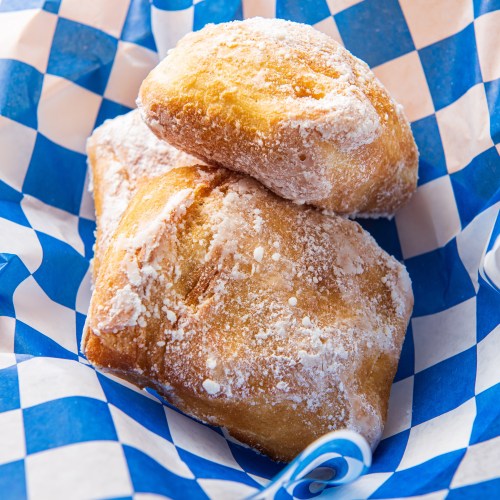 Two powdered sugar-dusted pastries stacked in a blue and white checkered basket.