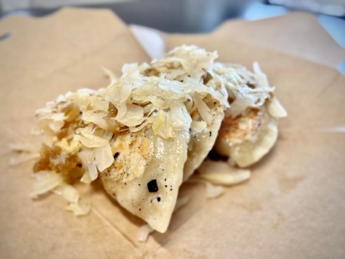 Three dumplings topped with sautéed cabbage on a brown paper surface.