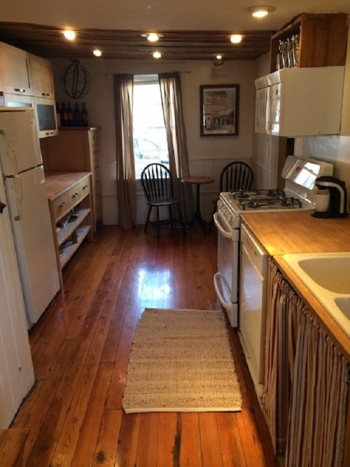 Cozy kitchen with wooden floors, white appliances, a small dining table, and natural light from a window.
