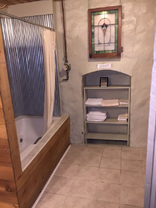 A rustic bathroom featuring a tub with a shower curtain, a stained glass window, and a shelf with neatly stacked towels.