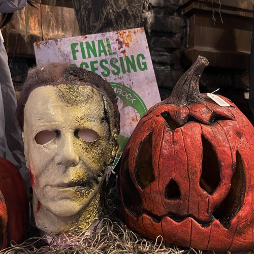 A creepy Halloween display featuring a Michael Myers mask and a carved pumpkin, set against a spooky backdrop.