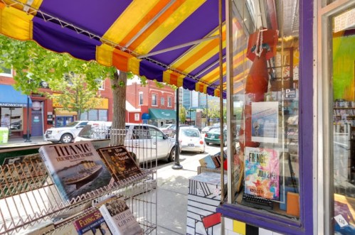 A colorful bookstore awning with books displayed outside, overlooking a vibrant street scene.