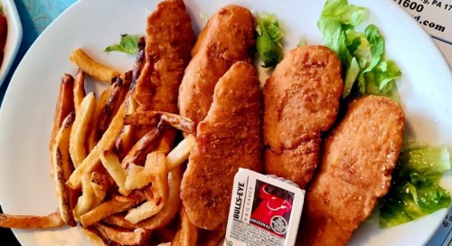 A plate of crispy chicken tenders with fries and lettuce, accompanied by a small container of barbecue sauce.
