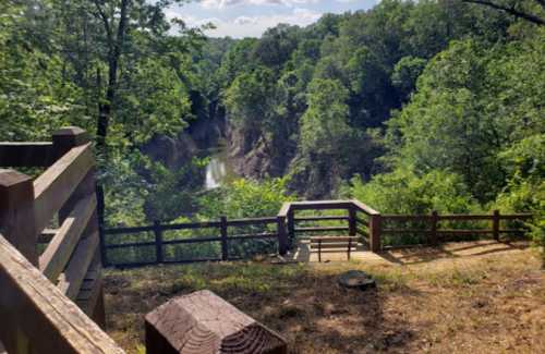 A scenic overlook with wooden railings, surrounded by lush green trees and a river winding through the valley below.