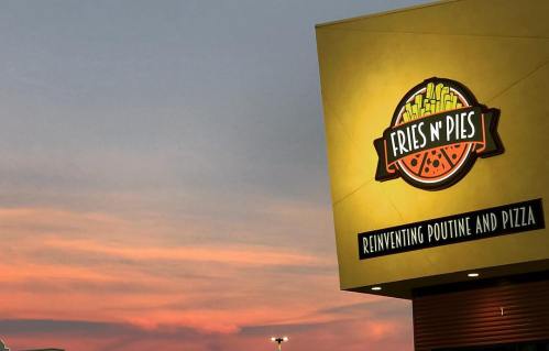 Sign for "Fries n' Pies" restaurant against a colorful sunset, promoting poutine and pizza.