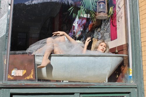A mannequin in a bathtub, wearing a tulle skirt, displayed in a shop window with a colorful backdrop.