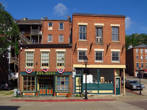 Two historic brick buildings with colorful storefronts, one featuring "Antiques" signage and patriotic decorations.
