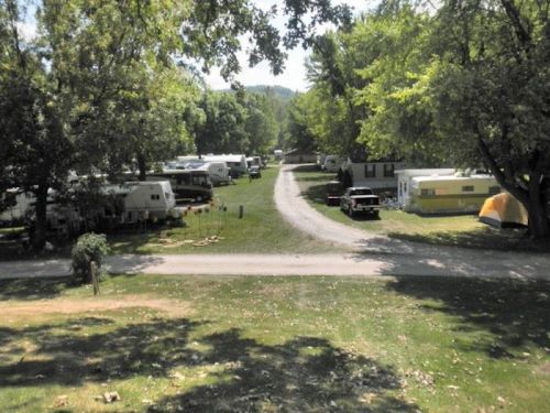 A scenic view of a campground with trailers, tents, and trees lining a winding road.