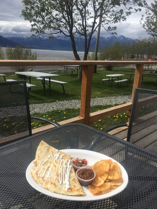 A plate of quesadillas with salsa and chips, set on a table with a scenic view of mountains and greenery.