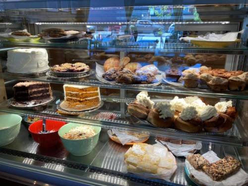 A display case filled with various baked goods, including cakes, pastries, and desserts in colorful bowls.
