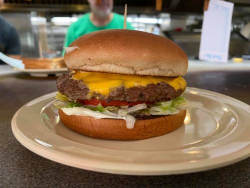 A cheeseburger with lettuce, tomato, and a slice of cheese on a toasted bun, served on a plate.