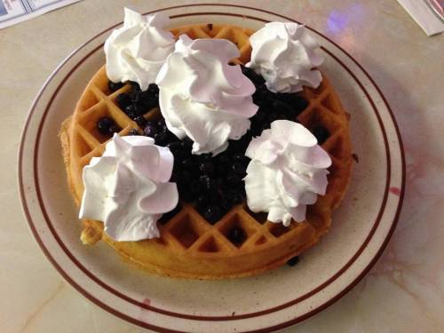 A golden waffle topped with blueberries and dollops of whipped cream on a plate.