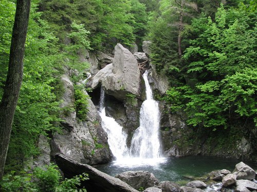 A serene waterfall cascading over rocks, surrounded by lush green trees in a tranquil forest setting.