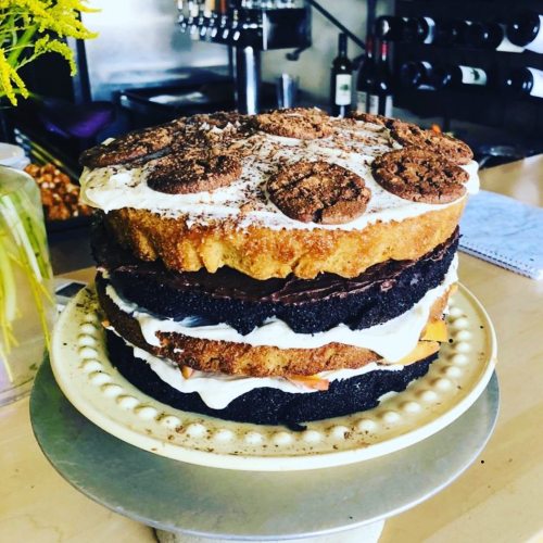 A tall, layered cake with chocolate and vanilla frosting, topped with cookies and chocolate shavings, on a decorative stand.