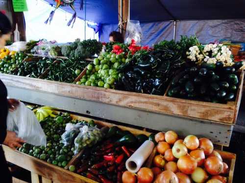 A vibrant market stall filled with fresh vegetables, including greens, peppers, limes, and onions.