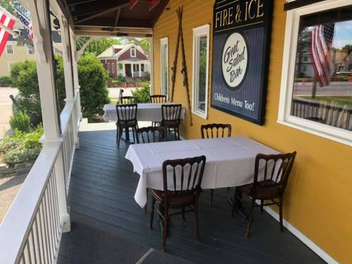 Outdoor dining area with empty tables and chairs on a porch, decorated with flags and a sign for "Fire & Ice."