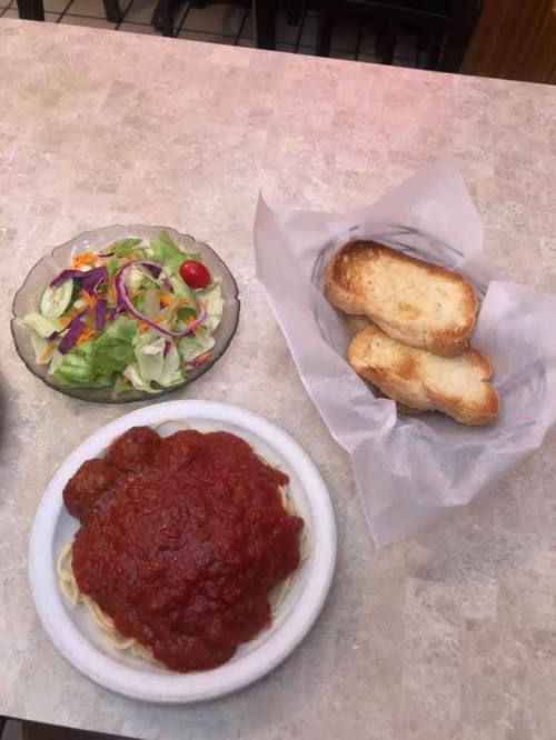 A plate of spaghetti with marinara sauce and meatballs, a side salad, and toasted bread on a table.