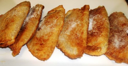 A plate of golden-brown fried pastries, lightly dusted with sugar, arranged in a row.