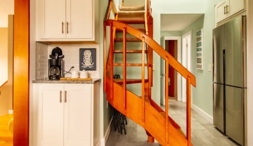 A wooden spiral staircase leads to an upper level, with a kitchen area featuring a coffee maker and modern appliances.