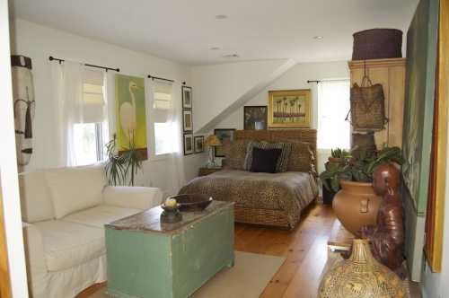 Cozy bedroom with a leopard-print bedspread, white sofa, plants, and artwork on the walls. Warm, inviting atmosphere.