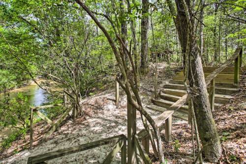 A wooded path leads to wooden stairs beside a creek, surrounded by lush greenery and trees.