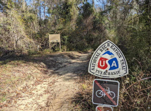 Trail sign for the National Recreation Trail in Tuxachanie, with a bike symbol and a wooden information board in the background.