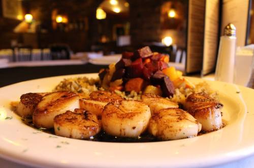 A plate of seared scallops served with a colorful vegetable medley and rice, set in a cozy restaurant ambiance.