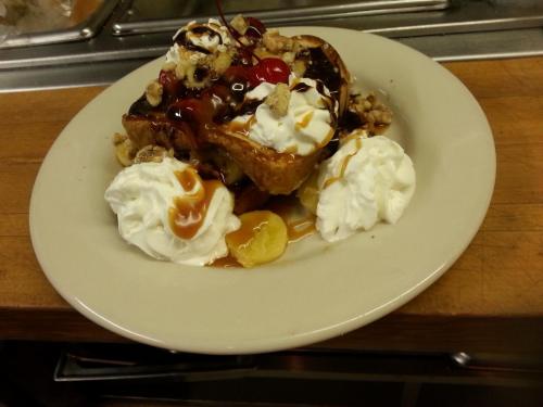 A plate of dessert featuring French toast topped with whipped cream, cherries, nuts, and drizzled with caramel sauce.