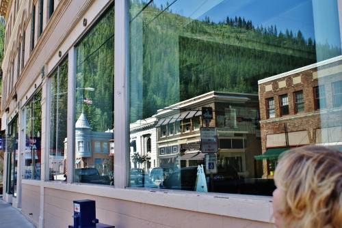 A reflection of buildings and trees in large windows, with a person in the foreground.