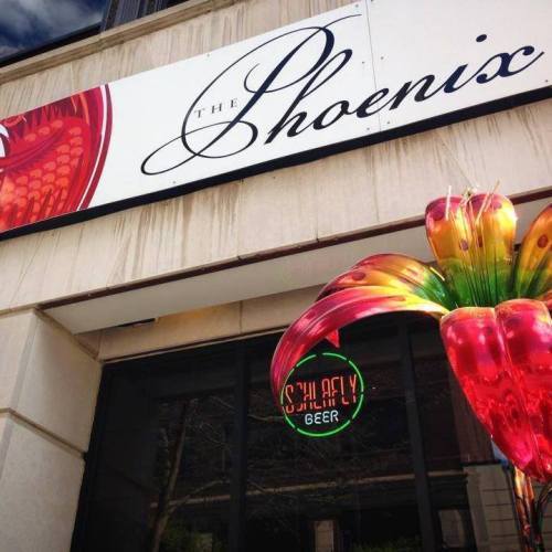Sign for "The Phoenix" with a colorful decoration and a neon "Schlafly Beer" sign in the window.
