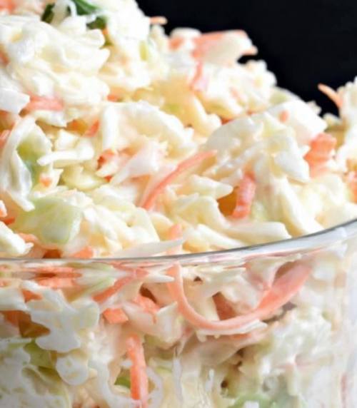 A close-up of creamy coleslaw with shredded cabbage and carrots in a glass bowl.