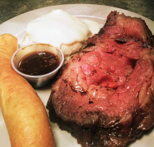 A plate featuring a slice of prime rib, creamy mashed potatoes, gravy, and a soft bread roll.