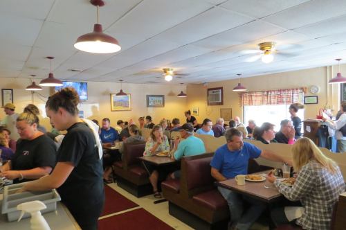 A busy diner filled with patrons at booths and tables, with a server attending to customers.