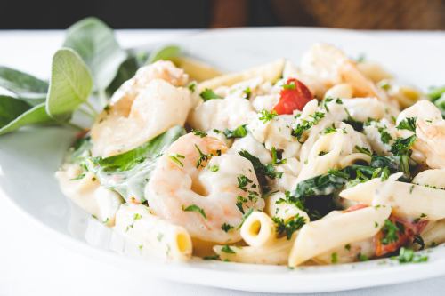 A plate of creamy pasta with shrimp, spinach, tomatoes, and herbs, garnished with fresh parsley.