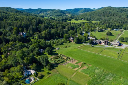 Aerial view of a lush green landscape with fields, farms, and rolling hills under a clear blue sky.