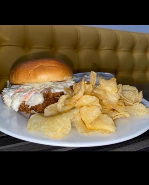 A plate with a fried chicken sandwich topped with mayo and a side of crispy potato chips.
