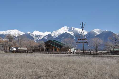 A wooden building with a sign reading "Ninepipes" in front of snow-capped mountains and a clear blue sky.