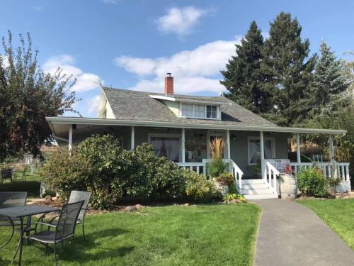 A charming green house with a porch, surrounded by trees and a well-kept lawn, under a blue sky with clouds.