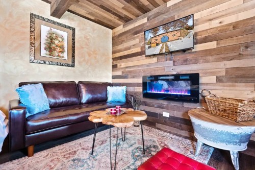 Cozy living room with a leather sofa, wooden walls, a modern fireplace, and a TV above a rustic coffee table.