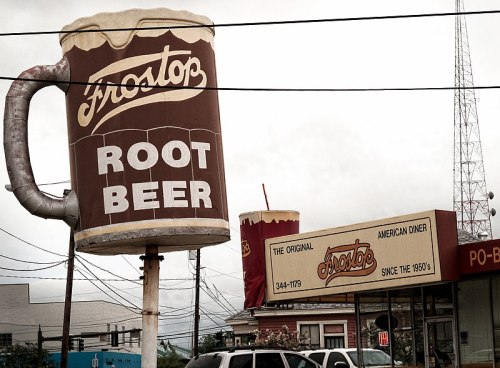 A large sign of a frosty root beer mug outside a diner, with a vintage style and a nearby telephone pole.