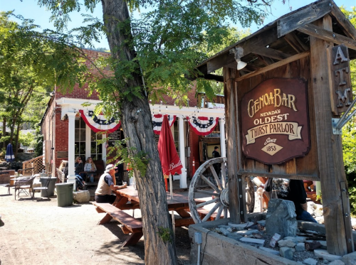 A rustic bar with a wooden sign, outdoor seating, and festive decorations in a historic setting.