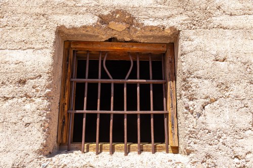A rustic window with a wooden frame and metal bars, set into a textured, earthen wall.