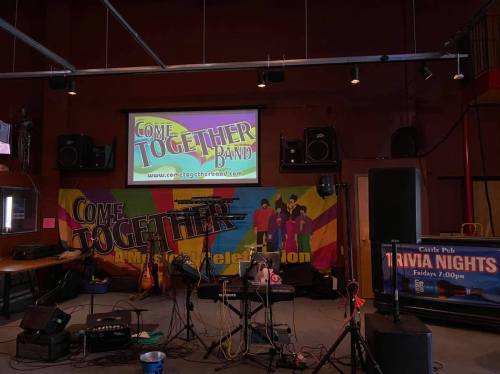 Stage setup for the "Come Together Band" with colorful backdrop, instruments, and a screen displaying the band's logo.