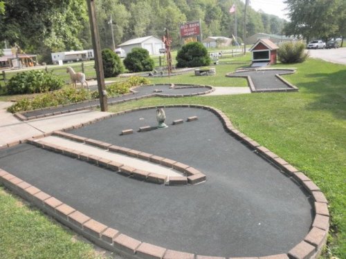 A mini-golf course with winding paths, surrounded by grass and trees, featuring decorative elements like a duck statue.