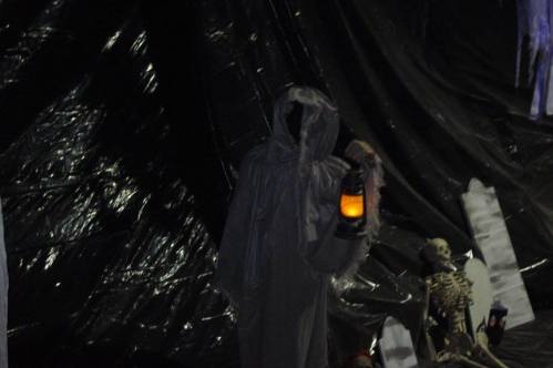 A ghostly figure in a white cloak holds a glowing lantern, with a skeleton visible in the background.